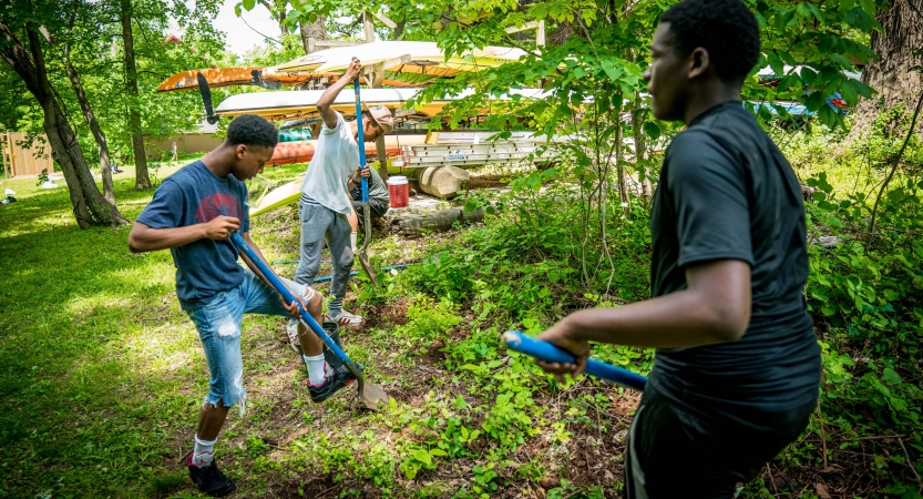Three young people use gardening tools during a service project with outward bound. 